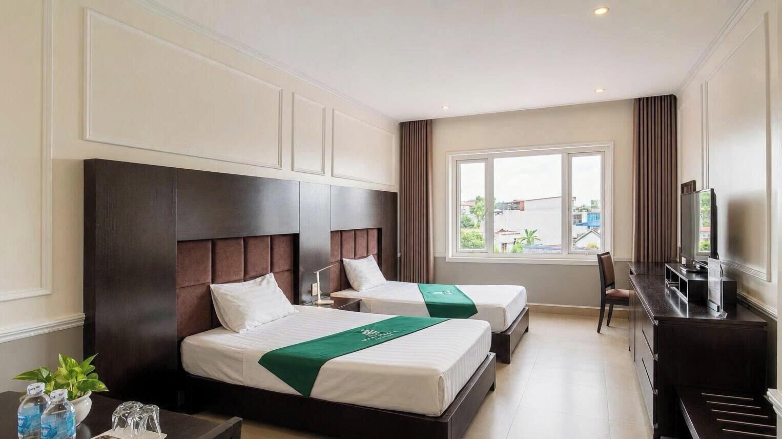 A hotel room with two beds, a desk, a chair, and a television.