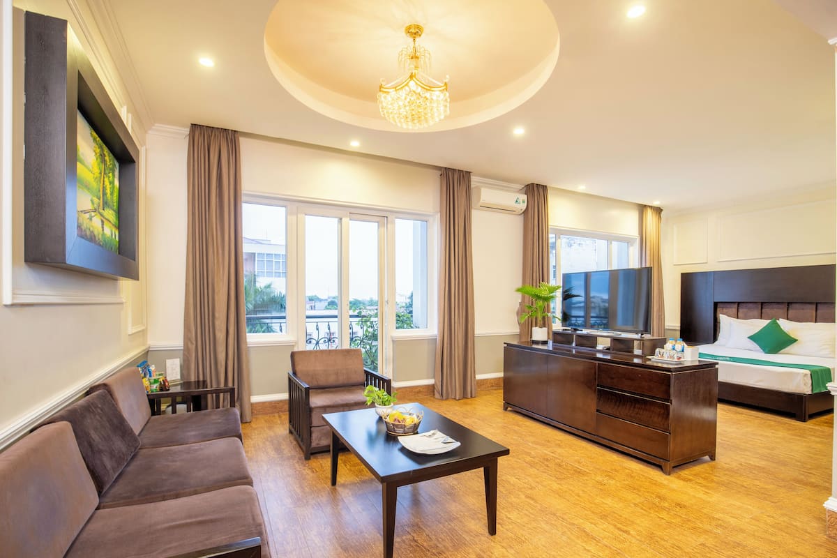 A hotel room with a sofa, a dining table, a TV, a bed, and a balcony with a view.