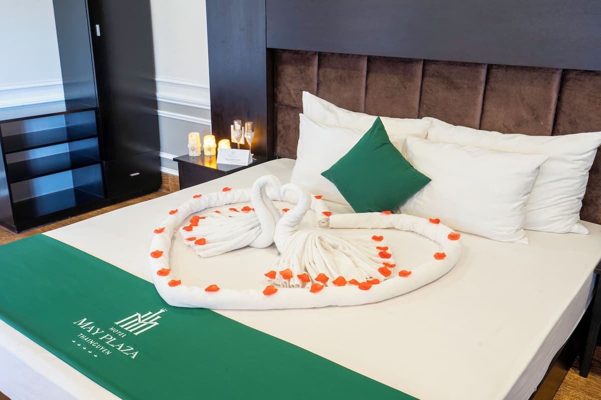 A hotel room with a neatly made bed, a green towel, and a swan-shaped towel decoration.
