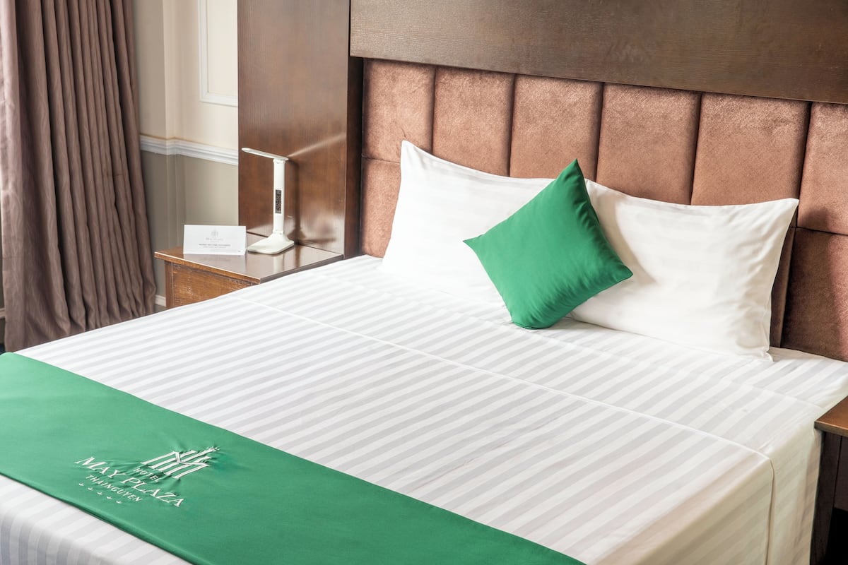 A neatly made bed with a green bedspread and a white pillow.