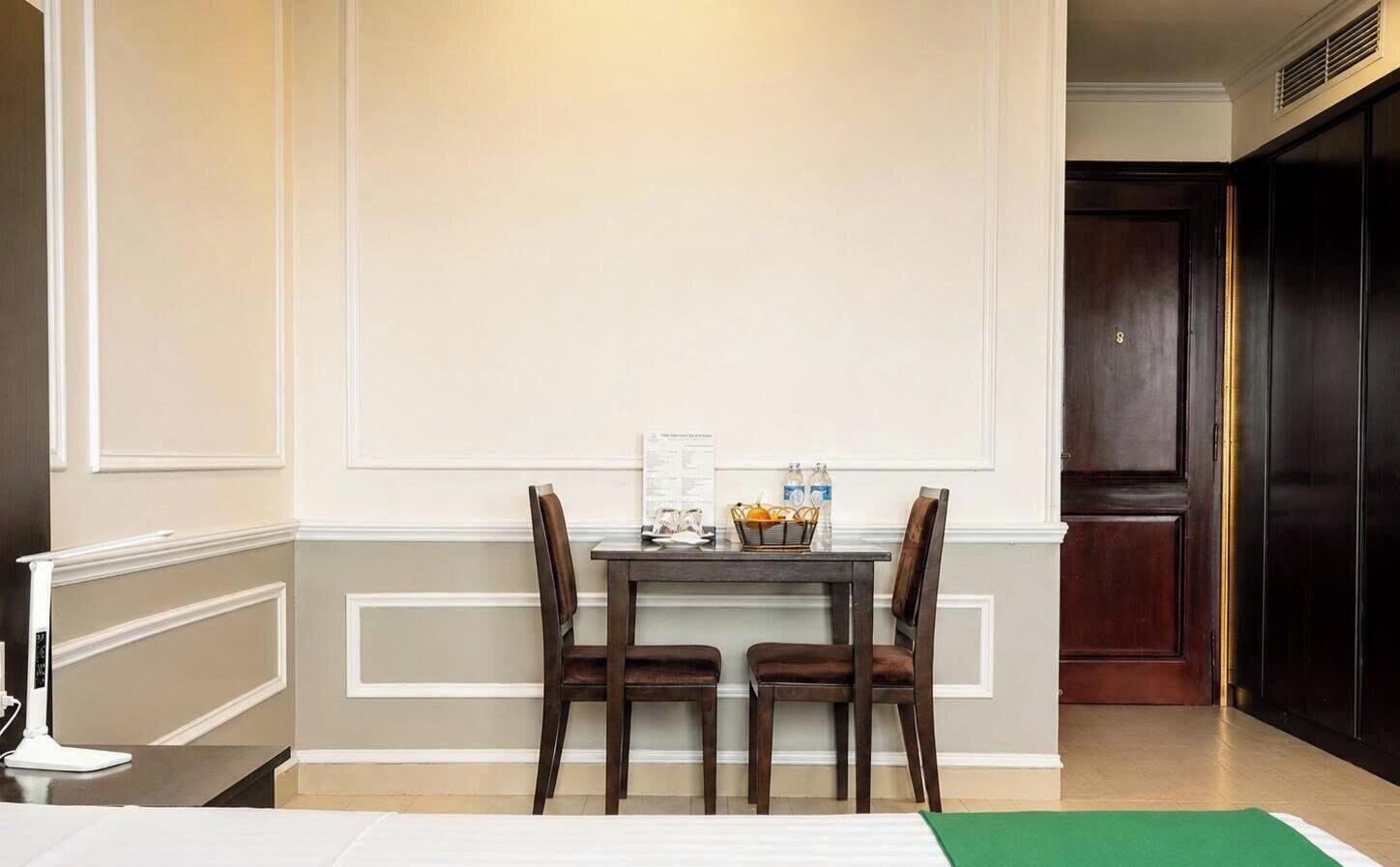A hotel room with a dining table set for two, a green area rug, and a dark wooden door.