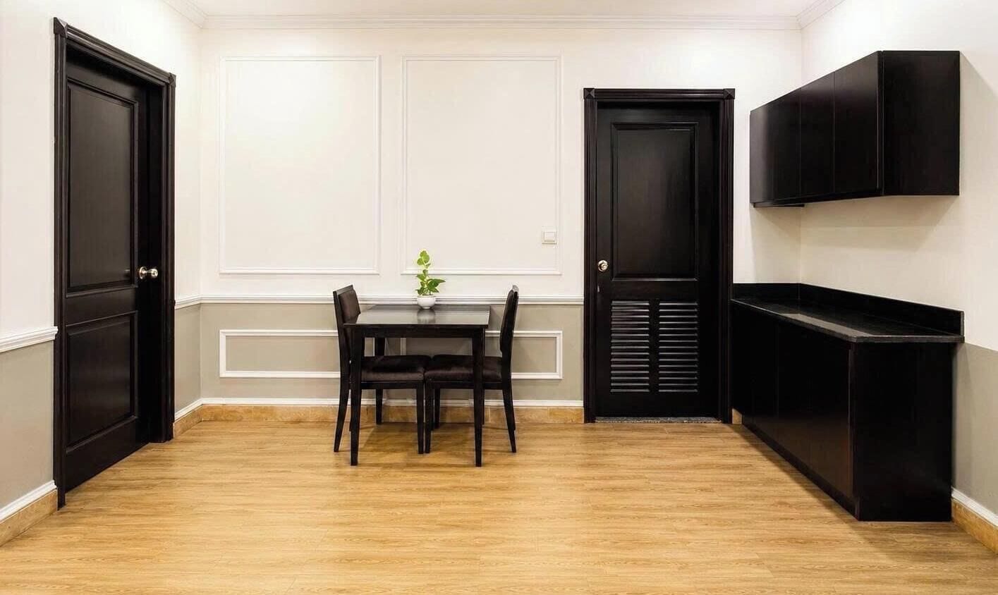 A room with a dining table and chairs, a black cabinet, and two black doors.