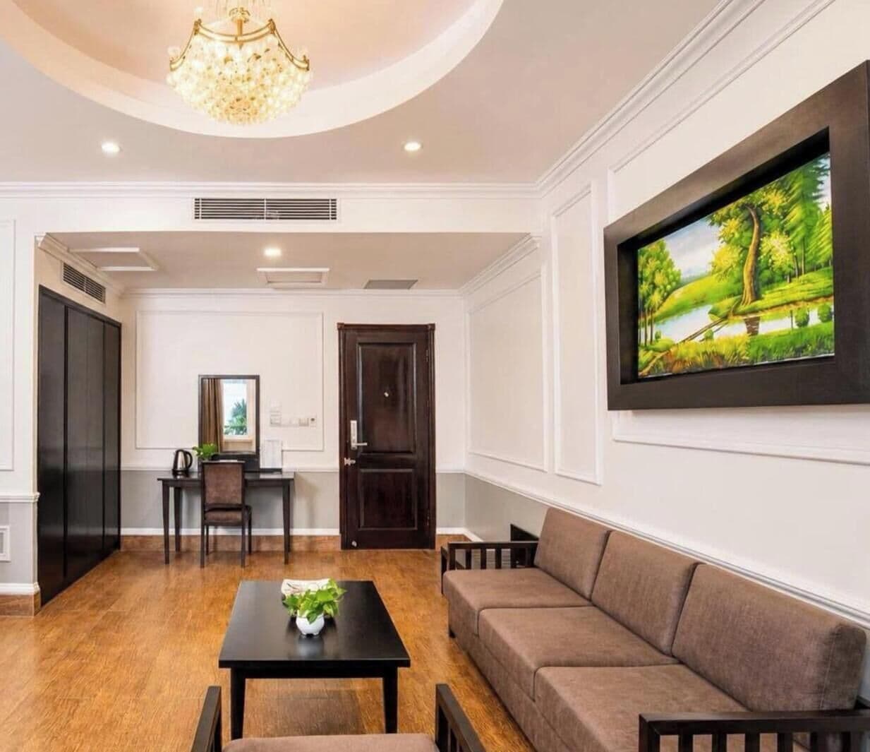 A room with a dark wooden door, a black table with a plant, a brown sofa, and a framed painting on the wall.