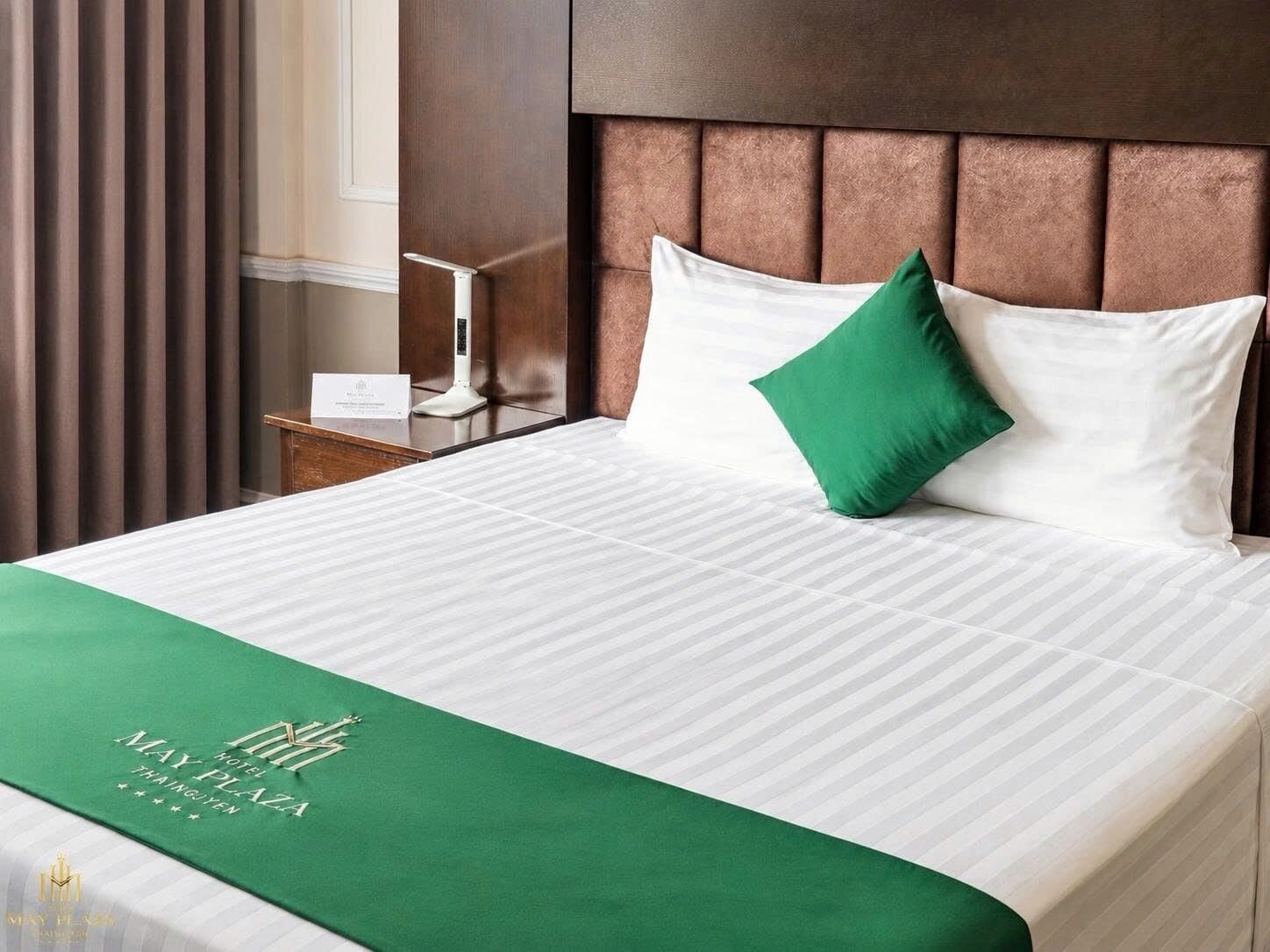 Une chambre d’hôtel avec un lit, une table de chevet, une lampe fixée au mur et une couvre-lit verte.