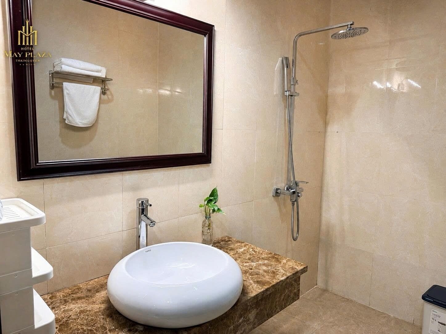 A bathroom with a round white sink, a mirror with a dark frame, a showerhead, and a towel rack.