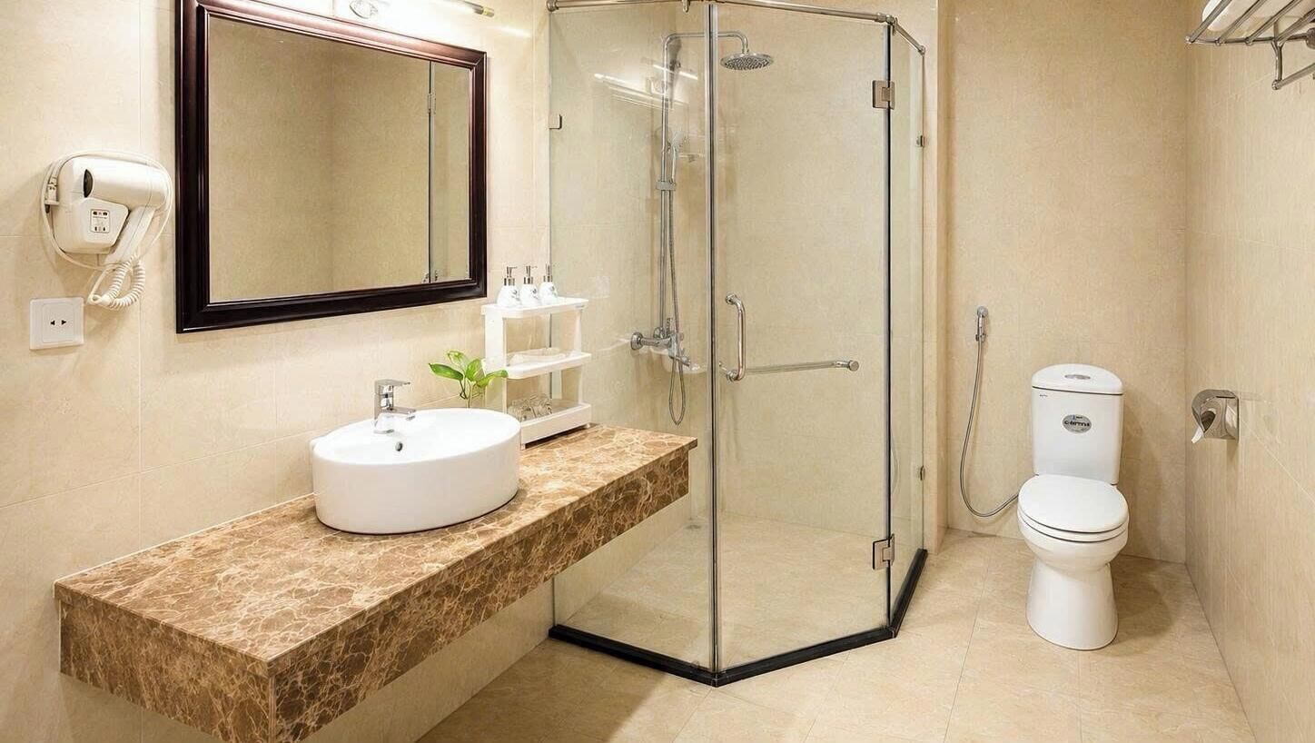 A bathroom with a glass-enclosed shower, a sink with a marble countertop, a toilet, and a mirror with a dark frame.