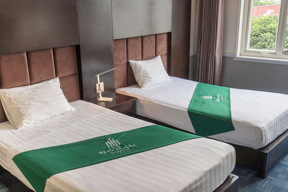 Two single beds with headboards, a bedside table with a lamp, and a window with curtains.