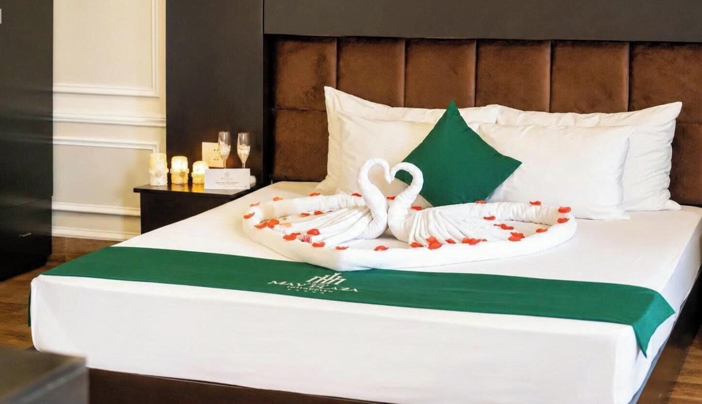 A neatly made bed with a swan-shaped towel arrangement, a green pillow, and a green bedspread.