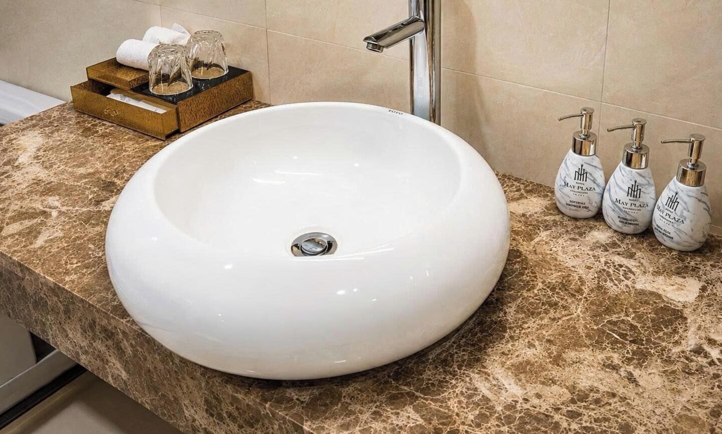 Un baño con un lavamanos grande de color blanco, una encimera de mármol y artículos de aseo a un lado.