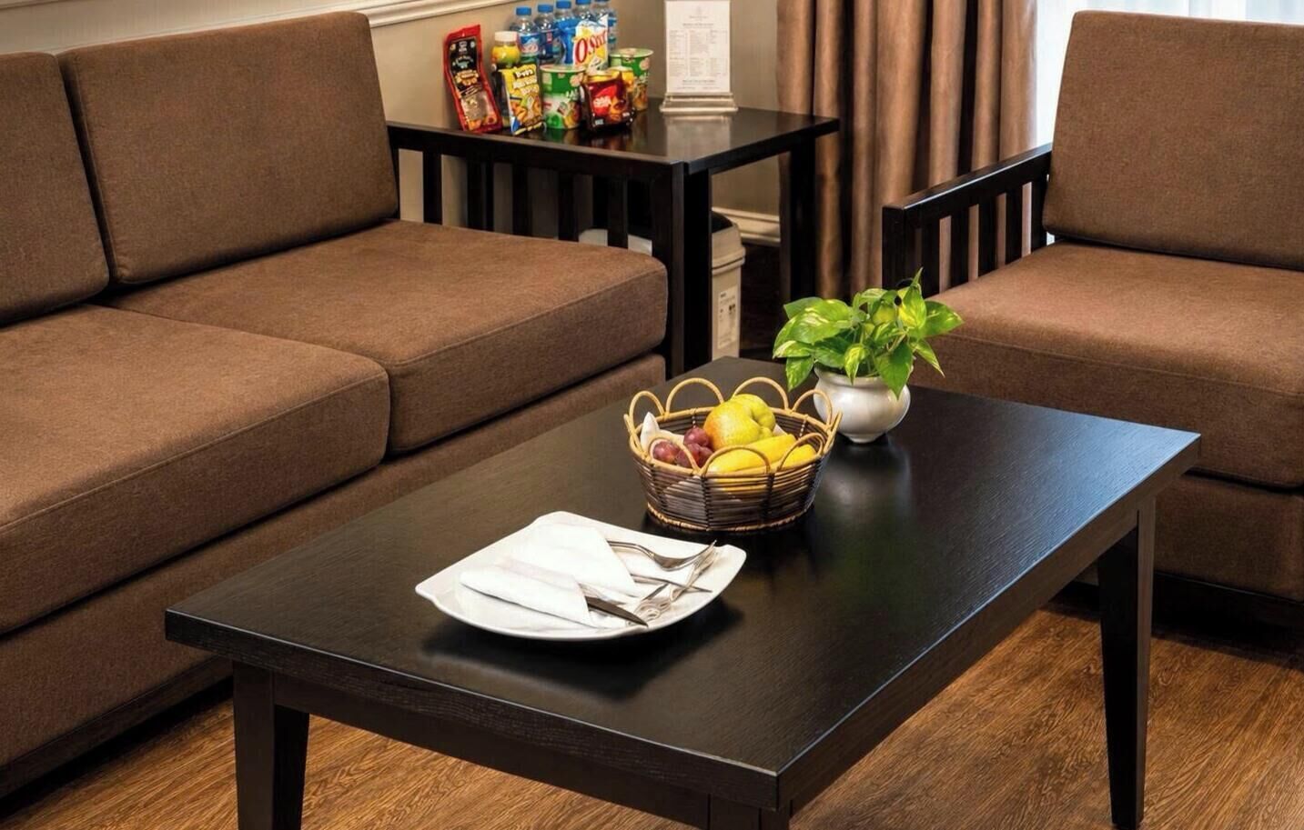 A modern living room with a dark wooden coffee table, a brown sofa, and a small table with snacks and a plant.