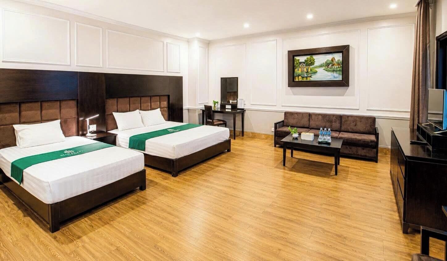 A hotel room with two beds, a sofa, a coffee table, a TV, and a painting on the wall.