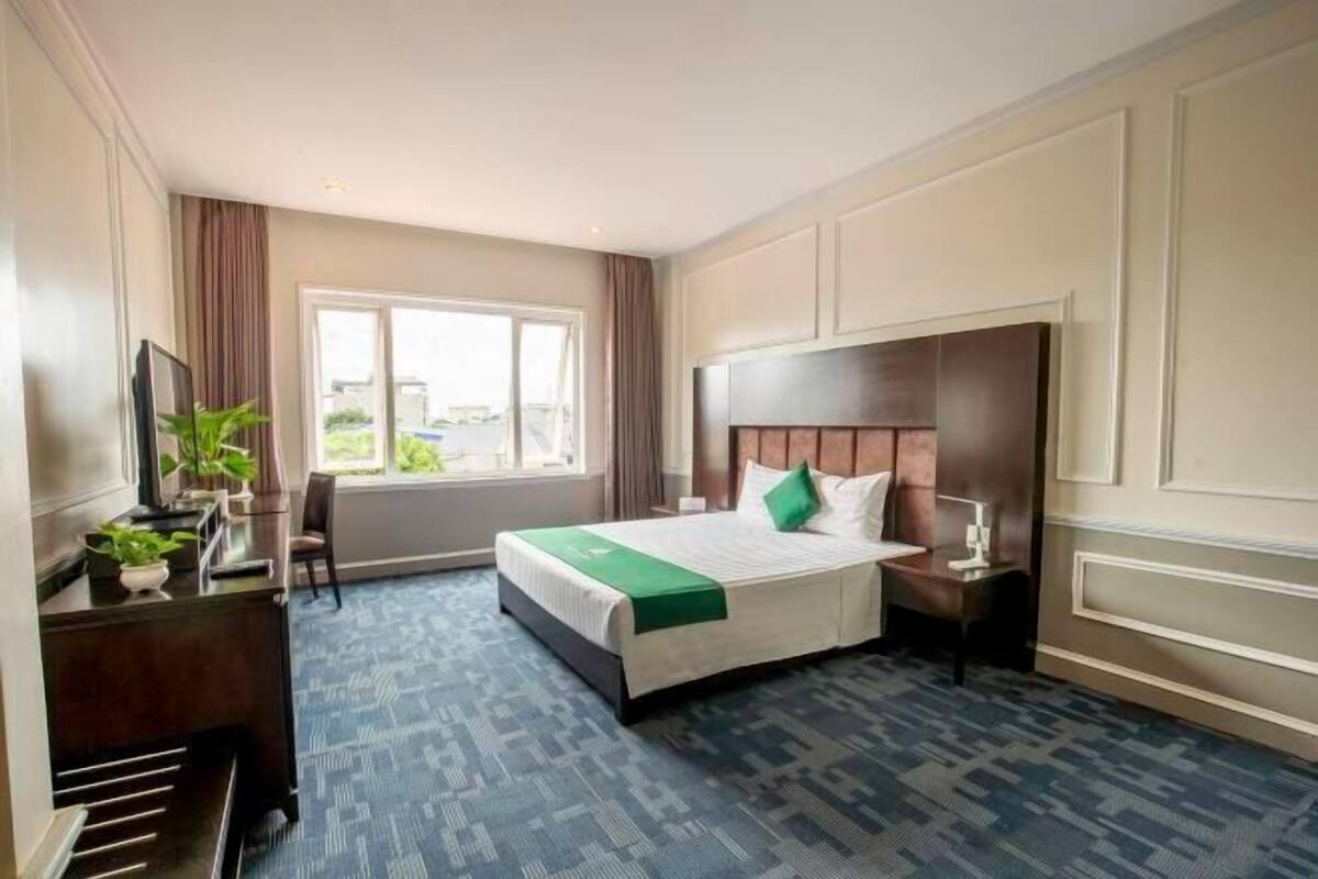 A hotel room with a large bed, a desk with a chair, a window, and a view of the outdoors.