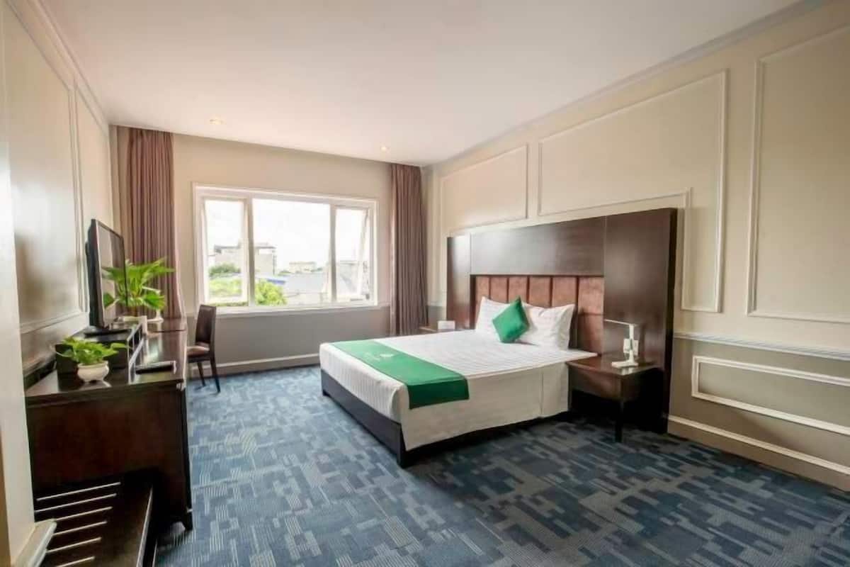 Quarto de hotel com uma cama grande, uma escrivaninha com cadeira, uma janela e vista para o exterior.