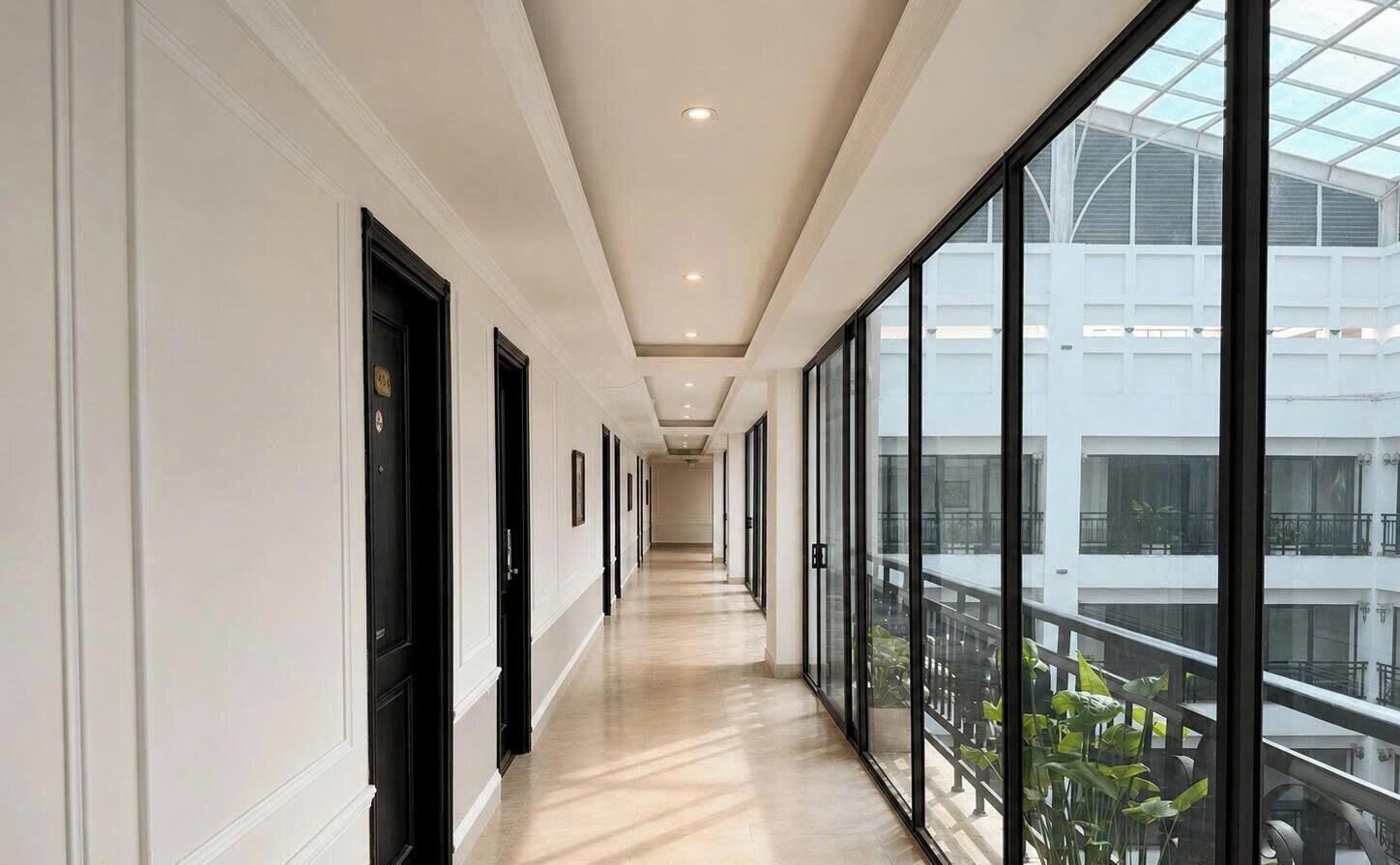 Un pasillo con puertas y ventanas de vidrio, que da a un balcón con plantas.