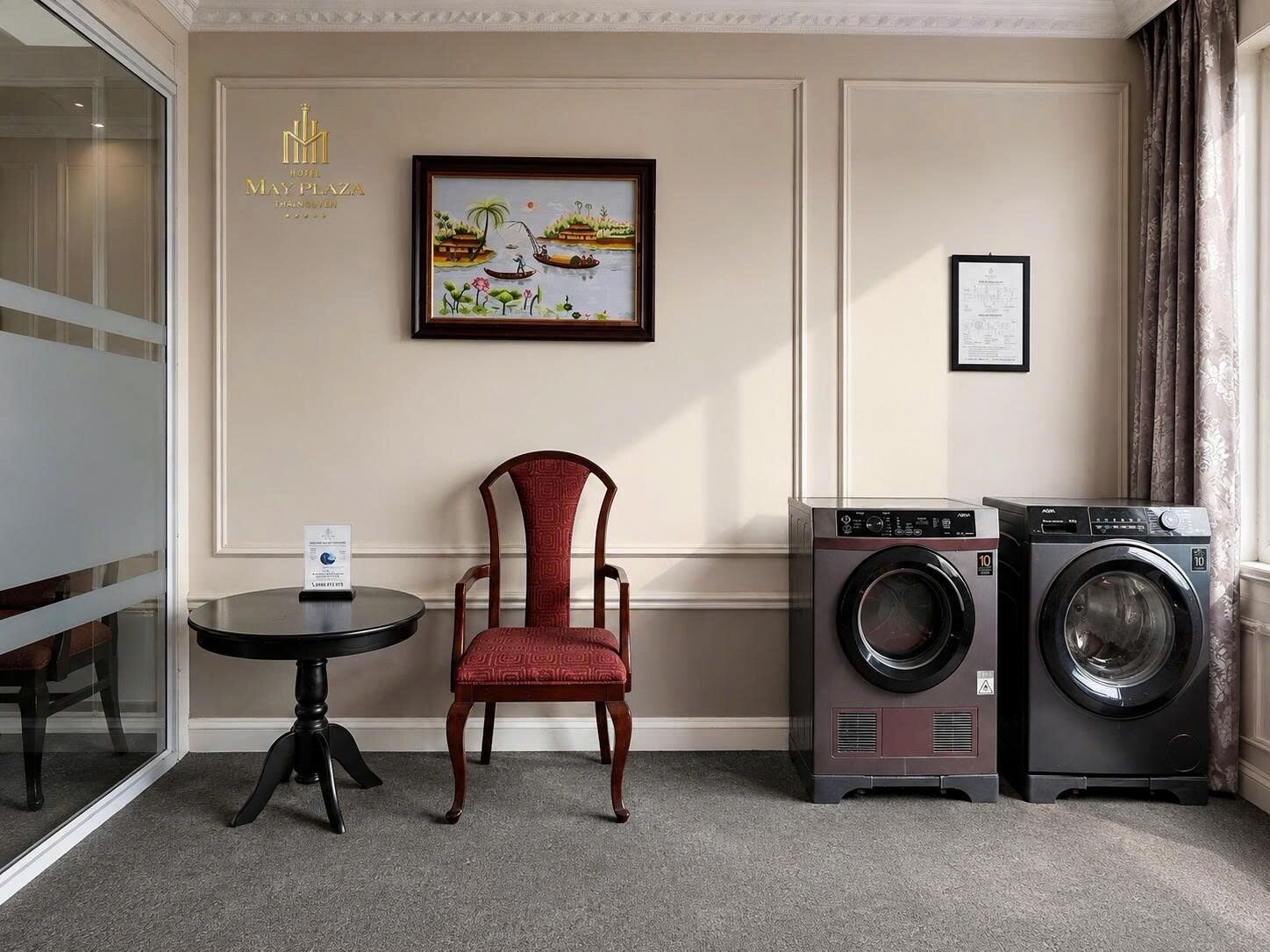 Une chambre d’hôtel avec une chaise, une table, un tableau encadré et un lave-linge.