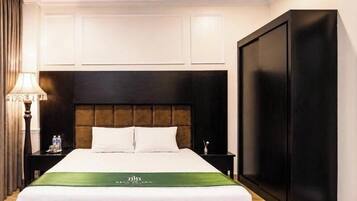 A hotel room with a large bed, a nightstand with a lamp, a wardrobe, and a wall-mounted air conditioning unit.