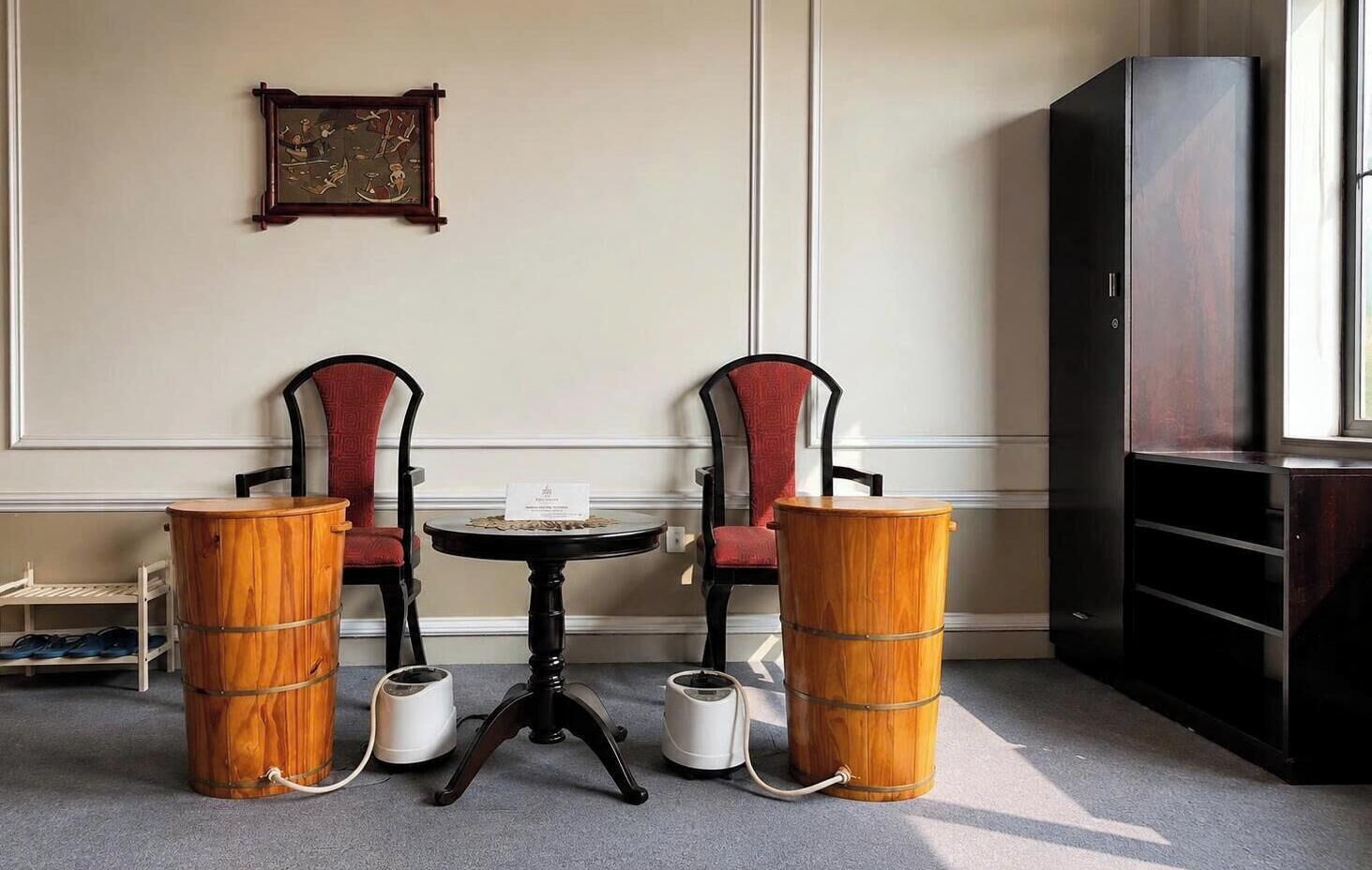 A room with two chairs, a small table, two wooden barrels, a television, and a framed picture on the wall.