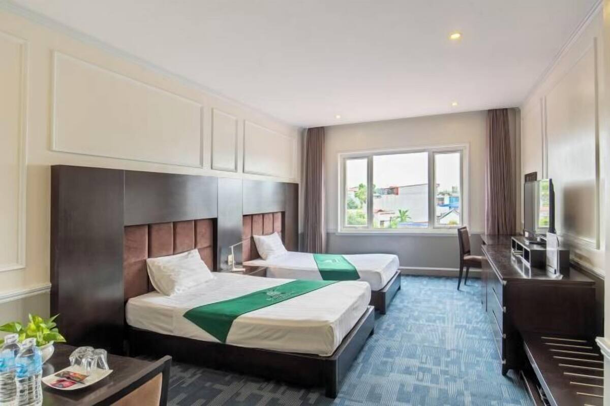 A hotel room with two beds, a desk, a chair, a TV, and a window with a view.