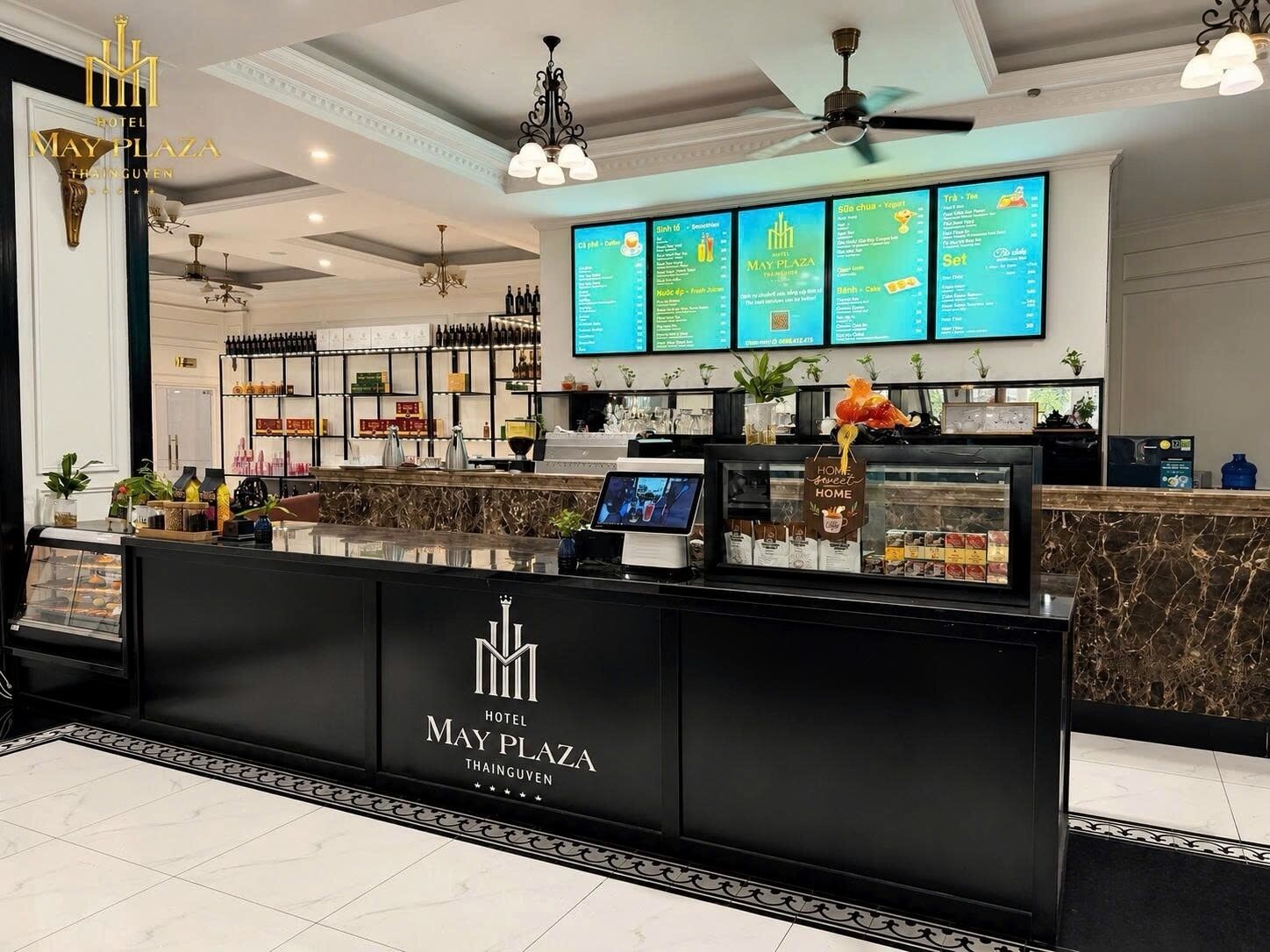 A hotel reception area with a black counter, a digital menu board, and a ceiling fan.