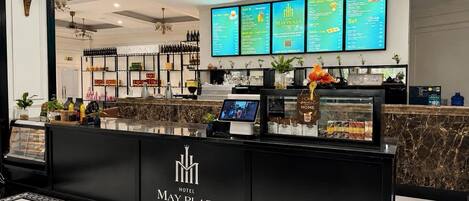 A hotel reception area with a black counter, a digital menu board, and a ceiling fan.