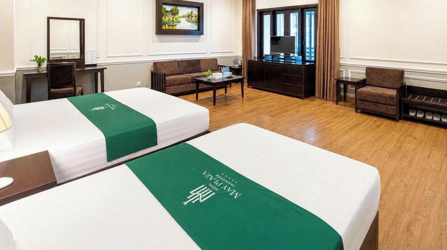 A hotel room with two beds, a sofa, a coffee table, a TV, and a shoe rack.