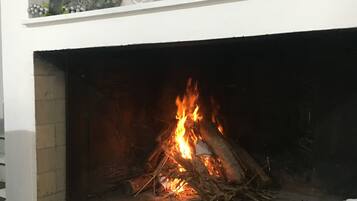 Una chimenea con fuego encendido, rodeada por una repisa blanca con una planta en maceta y un farol.