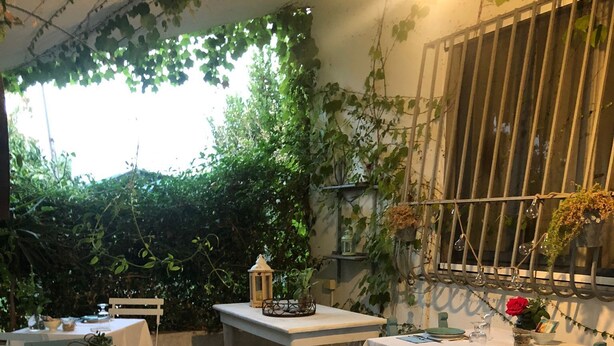 An outdoor dining area with tables set for two, surrounded by greenery and a rustic fence. - BeB il Pomo D'Oro (Assemini)