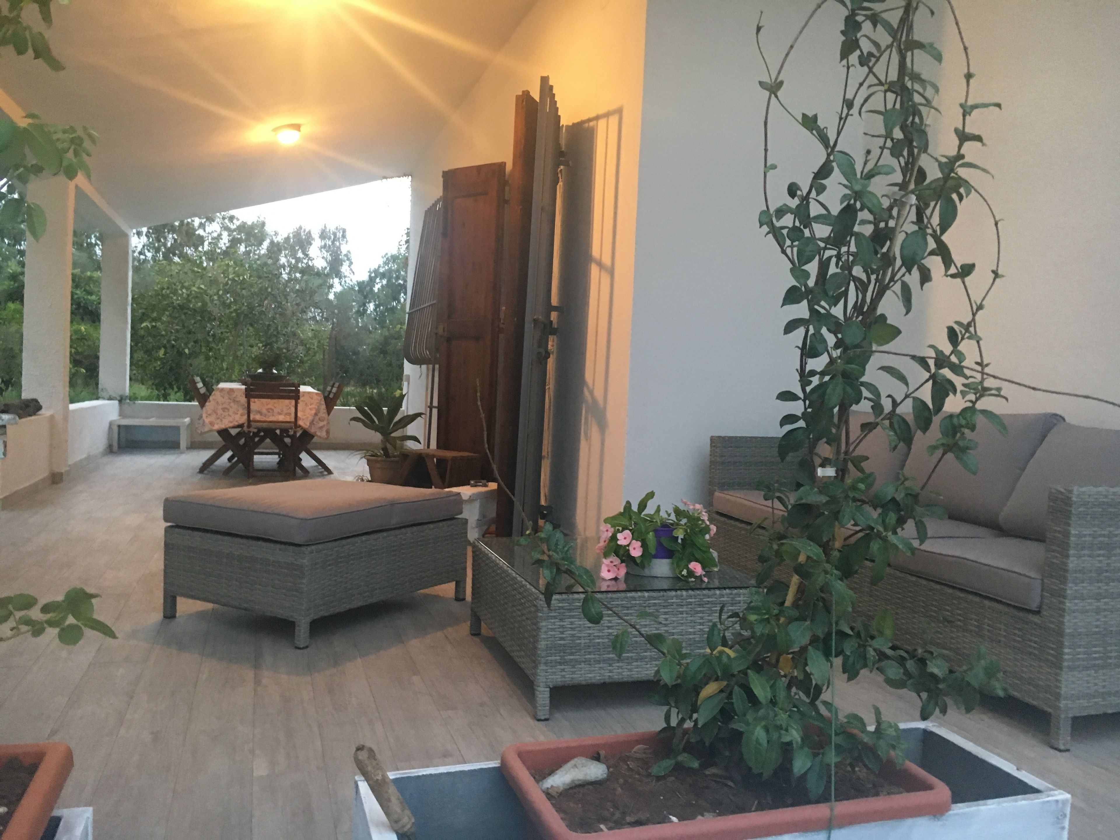 An outdoor patio with wicker furniture, a sofa, and potted plants.
