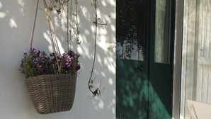 A white wall with a hanging basket of purple flowers, a green door, and a moss-covered stone planter. - BeB il Pomo D'Oro (Assemini)
