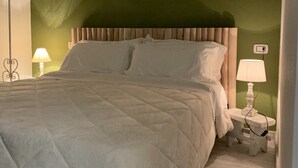 A neatly made bed with a quilted white duvet, a wooden headboard, and a nightstand with a lamp. - BeB il Pomo D'Oro (Assemini)