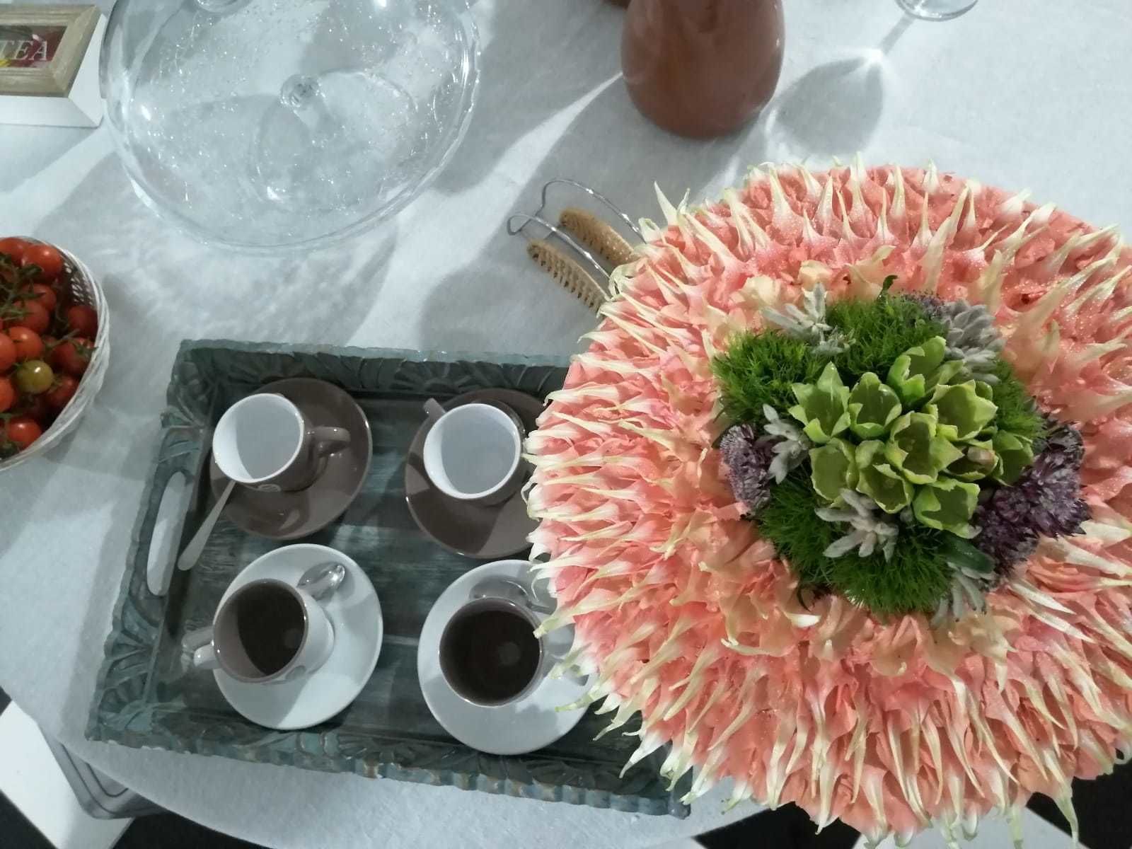 Una mesa con una bandeja que sostiene dos tazas de té, una jarrón de vidrio y un arreglo floral decorativo.