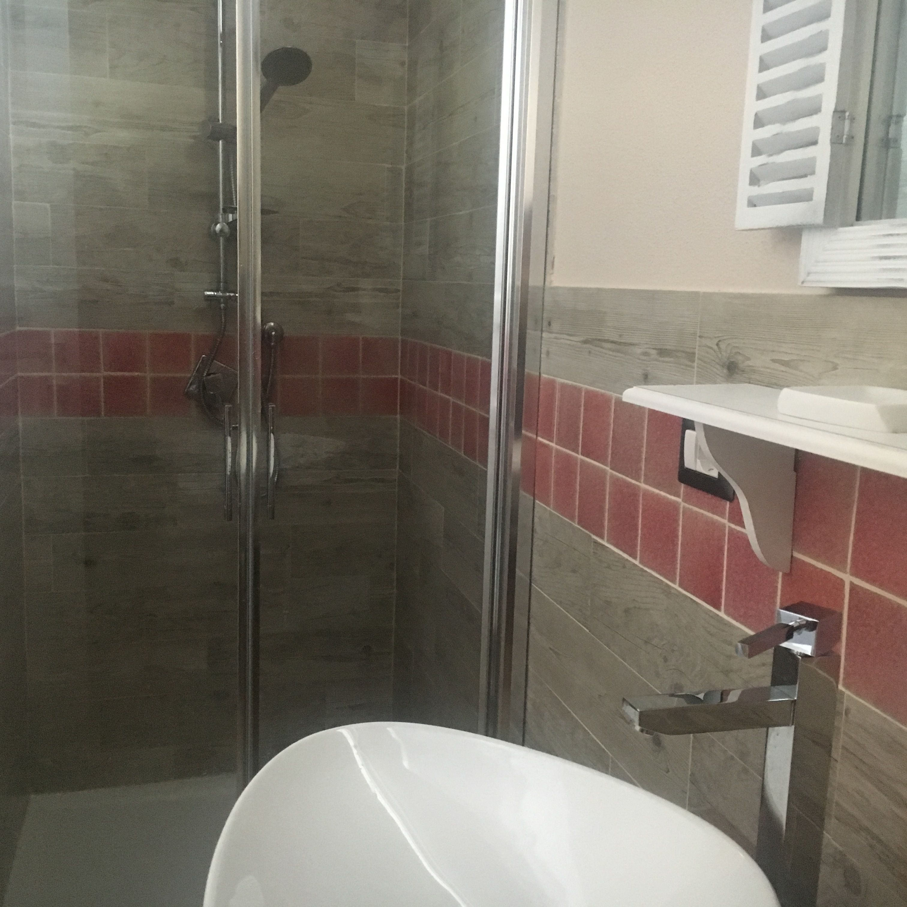 Una doccia con porta in vetro, un WC bianco e una parete rivestita di piastrelle rosse.