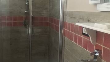 Una doccia con porta in vetro, un WC bianco e una parete rivestita di piastrelle rosse.