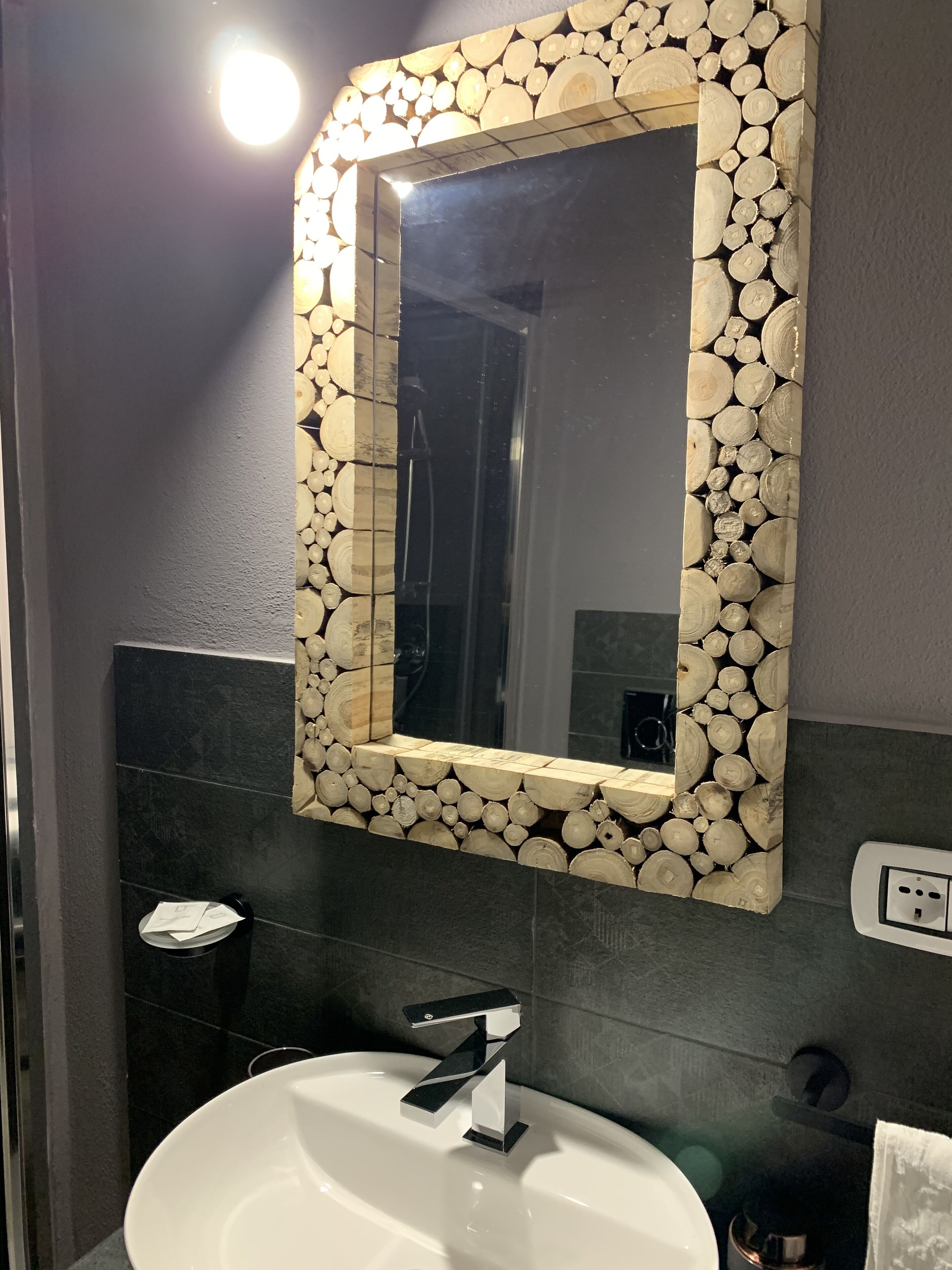 Une salle de bain avec un lavabo blanc, un robinet moderne et un miroir encadré d’un motif en bois et en pierre.