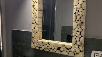 Une salle de bain avec un lavabo blanc, un robinet moderne et un miroir encadré d’un motif en bois et en pierre.