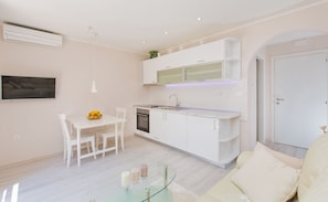 Una cocina moderna con muebles blancos, una mesa de comedor con sillas y una pequeña isla con encimera de vidrio.