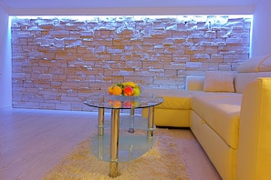Una sala de estar moderna con una mesa de centro de vidrio, una pared de piedra y un sofá amarillo.