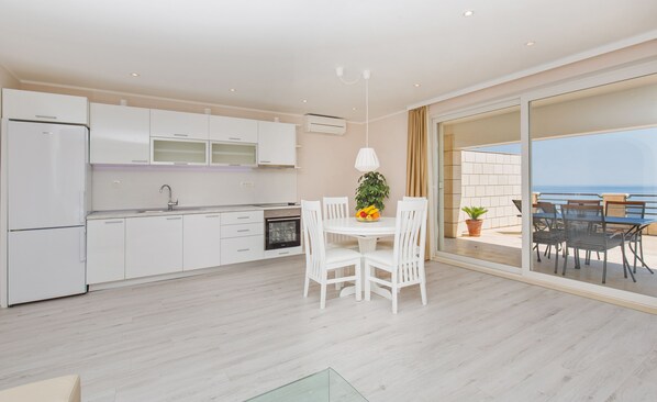 A modern kitchen with white cabinets, a dining area with white chairs, and a balcony with a view of the sea.