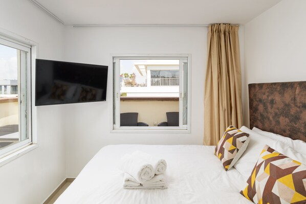 A hotel room with a bed, a TV mounted on the wall, a window with a view of the outside, and a balcony. - Penthouse with Panoramic View by FeelHome (Tel Aviv)