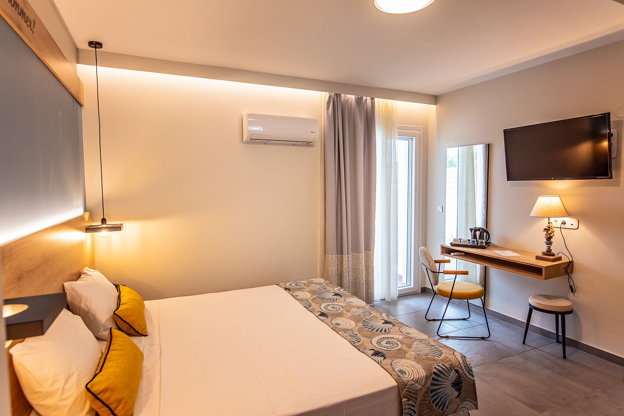 Habitación de hotel con cama, escritorio con silla, televisión montada en la pared y aire acondicionado.