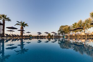 Une piscine aux eaux cristallines, bordée de chaises longues et d’ombrelles, et entourée de palmiers.