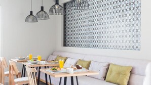 A breakfast setting with a sofa and dining tables, a patterned wall, and pendant lights. - Mythic Summer Hotel (Katerini)