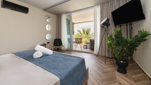 A hotel room with a bed, a chair, a TV, a plant, and a balcony with a view. - Mythic Summer Hotel (Katerini)