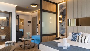 A modern hotel room with a large bed, a blue armchair, a small table with a vase, and a mirror. - Mythic Summer Hotel (Katerini)