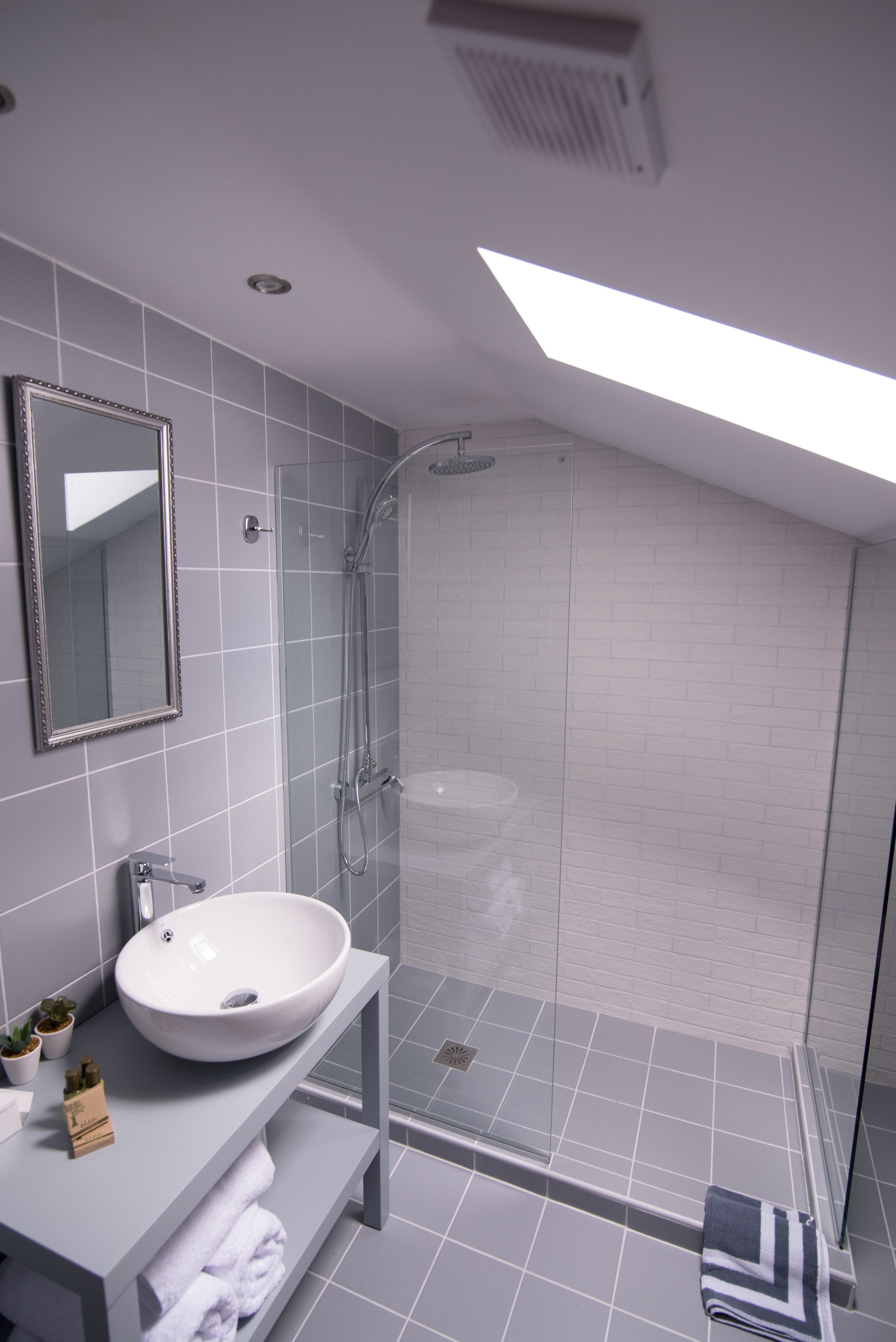 A modern bathroom with a large white sink, a glass shower enclosure, and a skylight.
