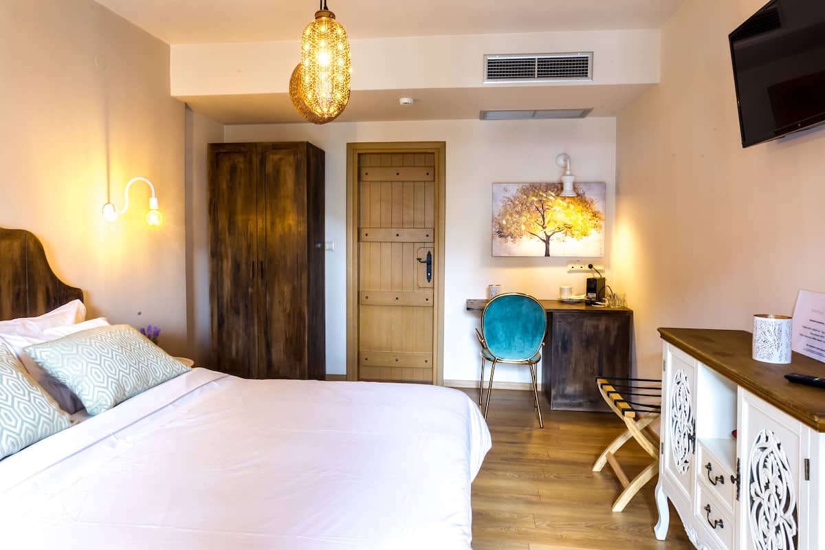 A bedroom with a bed, wooden wardrobe, desk, chair, and a television on the wall.