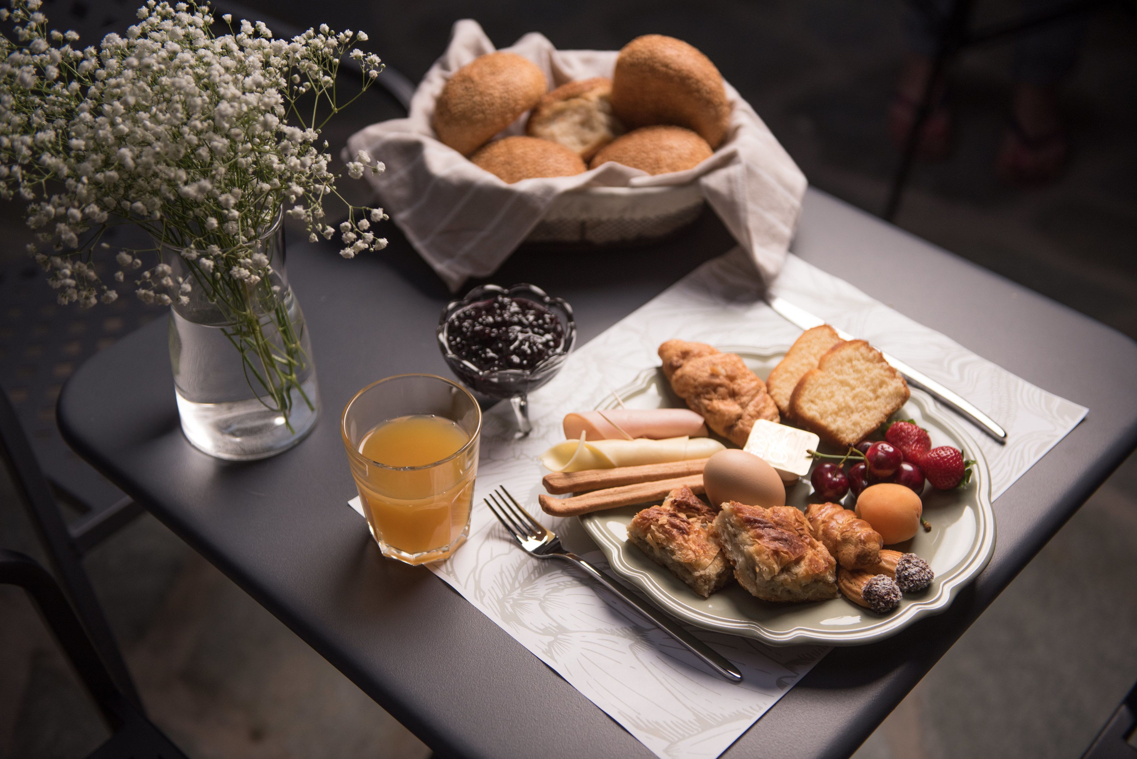Ett frukostbord med en tallrik mat, ett glas apelsinjuice, en skål med bär, en vas med blommor och en korg med frallor.
