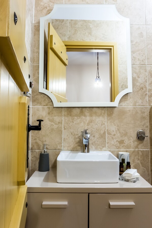 Un baño con un lavamanos blanco, un espejo y azulejos color beige.