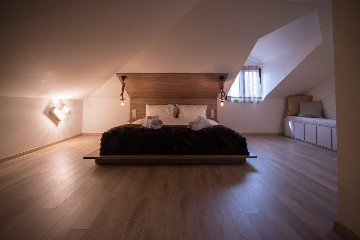 A bedroom with a sloped ceiling, a wooden headboard, a large bed with a fluffy rug, and a small seating area with a bench and cushions.