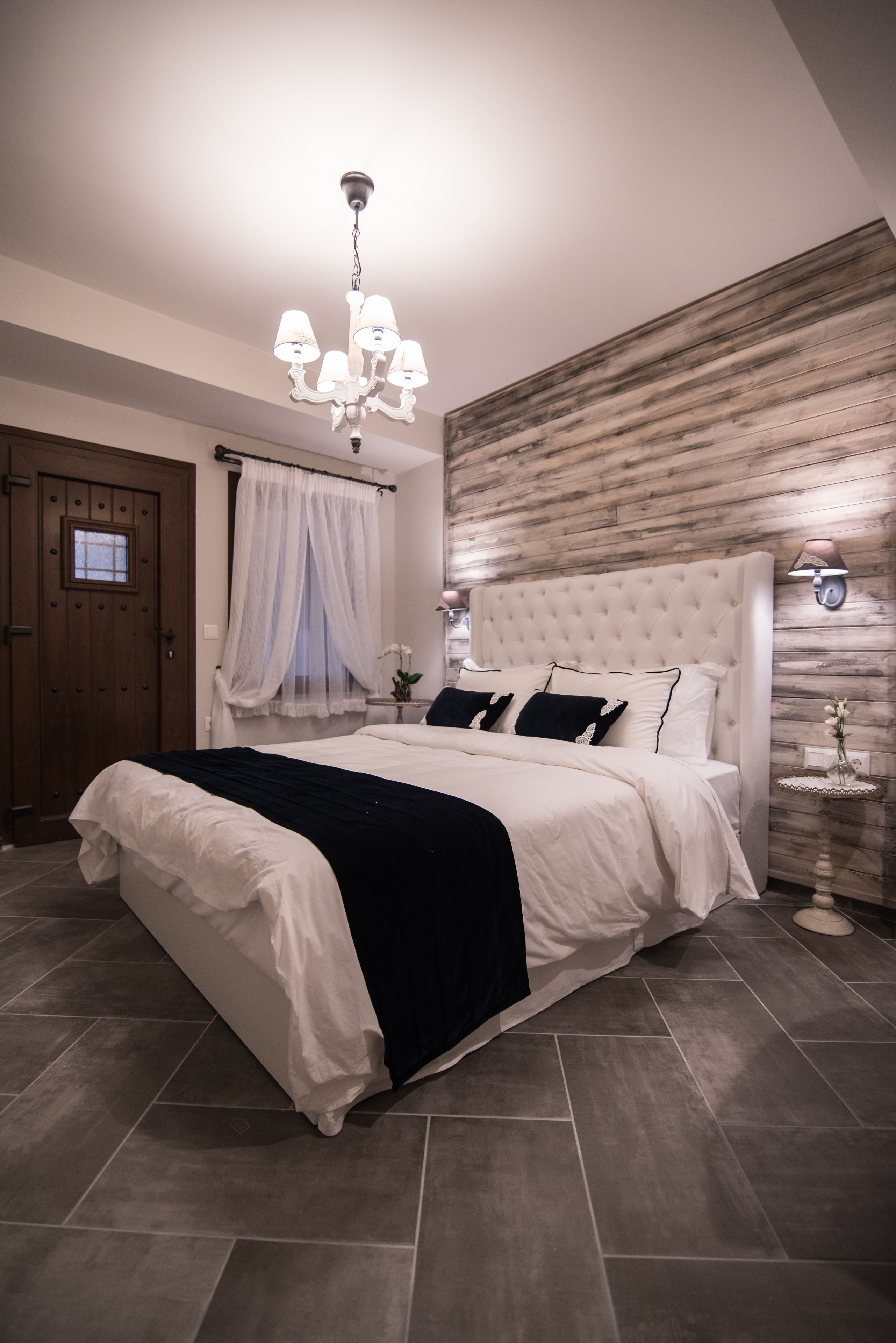 A bedroom with a large bed, a chandelier, a wooden wall panel, and a nightstand with a lamp.